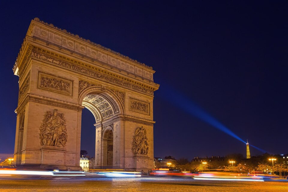 Arc de Triomphe illuminé de nuit avec des lumières de circulation en arrière-plan.